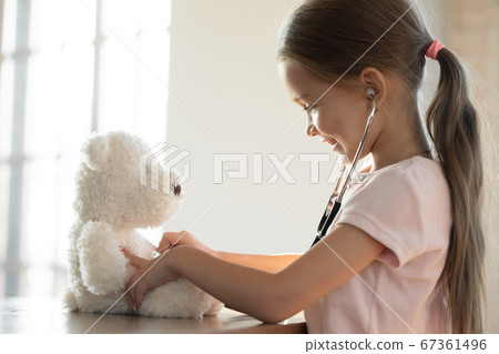 Smiling little girl using stethoscope, playing with fluffy toy 67361496