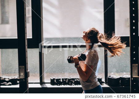Slender athletic girl performs physical exercises with dumbbells. Slender athletic girl performs physical exercises with dumbbells. 67361745