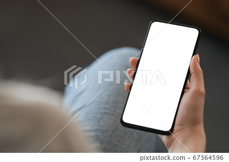 Young woman hold smarphone with white screen while sitting in a chair 67364596