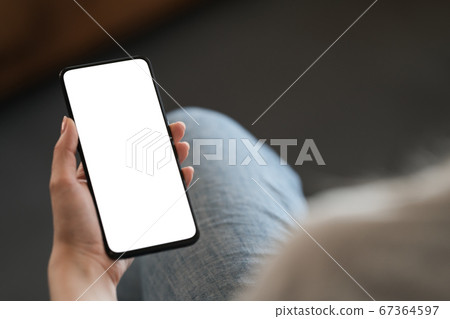 Young woman hold smarphone with white screen while sitting in a chair Young woman hold smarphone with white screen while sitting in a chair 67364597