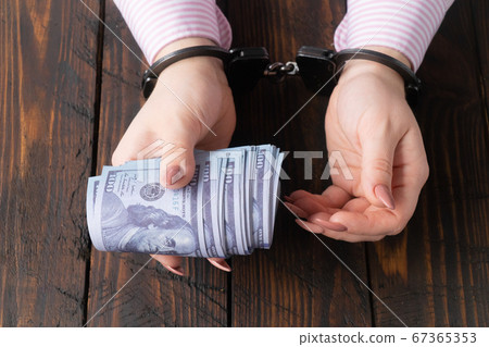 female hands in handcuffs hold twisted money on a dark wooden background 67365353