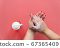 Woman soaps hands with liquid soap on pink background 67365409