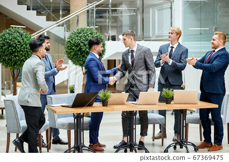 Arabic and caucasian businessmen in tuxedos shaking hands after negotiation 67369475