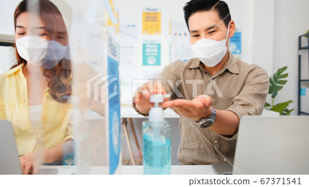 Asian business people wear face mask, wash hand use hand sanitizer, and separated by partition stand 67371541