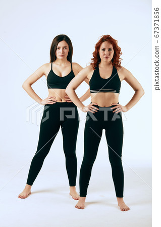 Two caucasian women are stand together in black tank tops and leggings on white Two caucasian women are stand together in black tank tops and leggings on white 67371856