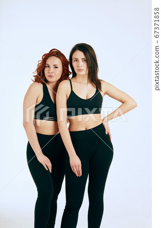 Two caucasian women standing together in black tank tops and leggings on white Two caucasian women standing together in black tank tops and leggings on white 67371858