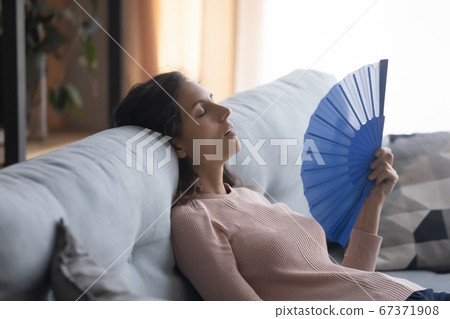 Overheated young woman waving with hand fan at home 67371908