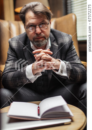 Mid-age businessman sits at table and thinks over his notes in notepad in office 67372275