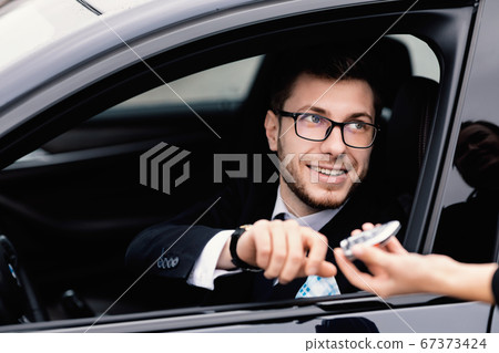 Bearded man taking auto key, sitting on driver's seat Bearded man taking auto key, sitting on driver's seat 67373424