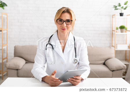 Online conference from home. Serious woman in white coat with tablet in hands Online conference from home. Serious woman in white coat with tablet in hands 67373872