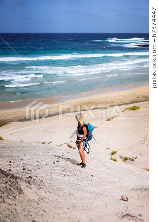 Woman hiker with backpack going down a sand dune towards the lonely beach. Sao Vicente Cape Verde 67374447