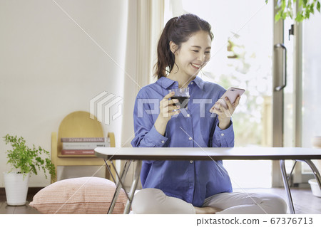 Young woman looking at smartphone while drinking ice coffee in living room 67376713