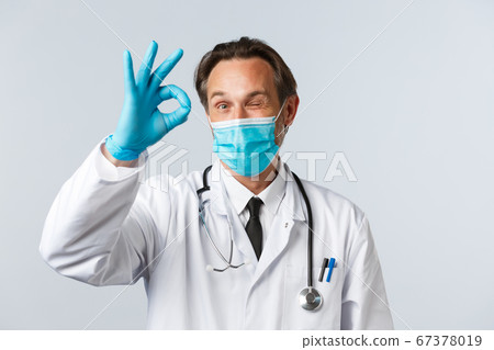 Covid-19, preventing virus, healthcare workers and vaccination concept. Cheerful satisfied doctor in medical mask and gloves show okay sign and wink. Physician give approval, agree with patient Covid-19, preventing virus, healthcare workers and vaccination concept. Cheerful satisfied doctor in medical mask and gloves show okay sign and wink. Physician give approval, agree with patient 67378019