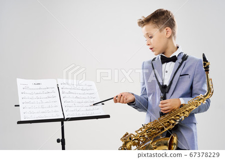 A boy in a classic suit with a saxophone considers notes  67378229