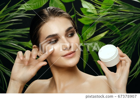 woman near green leaves with cream in a jar woman near green leaves with cream in a jar 67378907