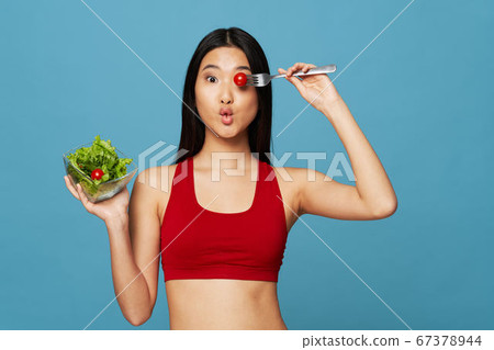 Slender woman with a plate of salad in hand and a tomato on a fork  67378944