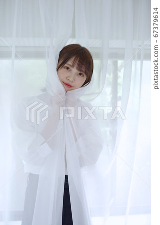 年輕女子把她的臉從花邊窗簾 67379614