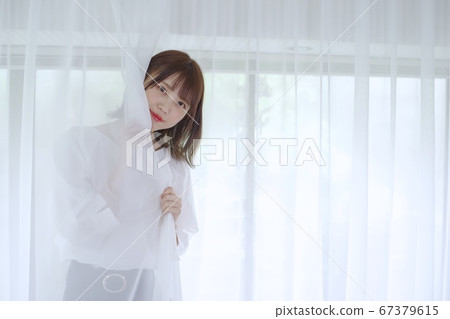 年輕女子把她的臉從花邊窗簾 年輕女子把她的臉從花邊窗簾 67379615