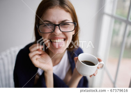 Cheerful woman with a cup of coffee shows tongue to the camera and glasses  67379616