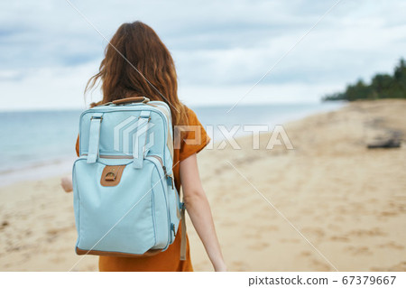 A woman in a yellow dress with a backpack on her back on the shore A woman in a yellow dress with a backpack on her back on the shore 67379667