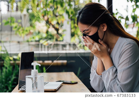 One 20s young adult business woman sneezing with tissue handkerchief. Casual female freelancer working with laptop outdoors with alcohol gel on desk. With copy space 67383133