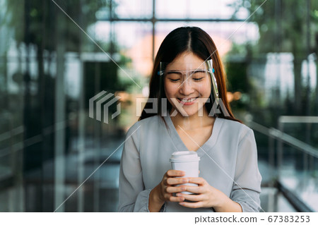 Young 20s Asian beautiful girl wearing a protective face shield and mask. Professional business woman holding a cup of coffee - Corona Virus prevention concept 67383253