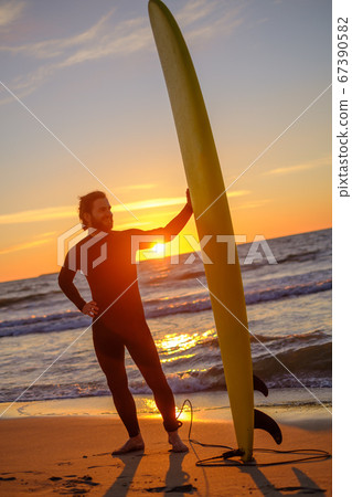 Bearded surfer on beach during sunset Bearded surfer on beach during sunset 67390582