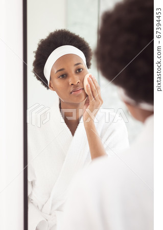 Woman applying makeup to her face while looking in the mirror Woman applying makeup to her face while looking in the mirror 67394453