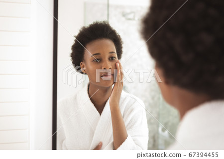 Woman applying moisturizer to her face while looking in the mirror Woman applying moisturizer to her face while looking in the mirror 67394455