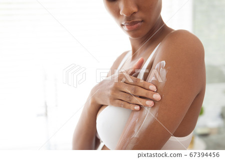 Woman applying moisturizer to her arms in bathroom Woman applying moisturizer to her arms in bathroom 67394456