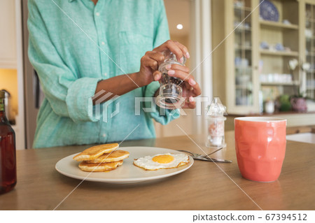 Mid section of woman putting salt on cooked eggs 67394512