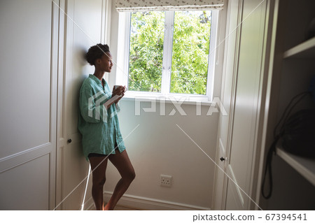 Woman drinking coffee while looking out of the window Woman drinking coffee while looking out of the window 67394541