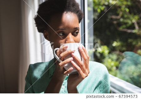 Woman drinking coffee while looking out of the window 67394573