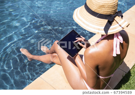 Woman using digital tablet while sitting by the pool Woman using digital tablet while sitting by the pool 67394589