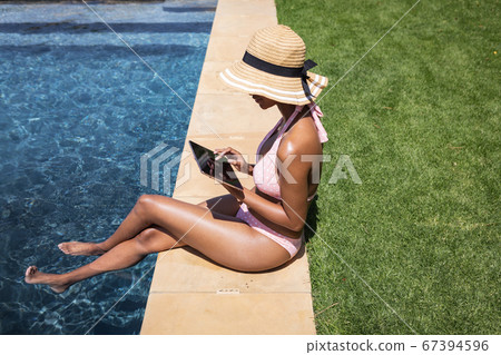 Woman using digital tablet while sitting by the pool Woman using digital tablet while sitting by the pool 67394596