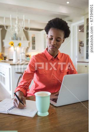Woman taking notes while using laptop in the kitchen Woman taking notes while using laptop in the kitchen 67394601