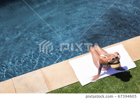 Aerial view of woman sunbathing by the pool 67394605