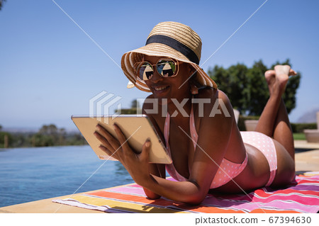 Woman using digital tablet while sunbathing Woman using digital tablet while sunbathing 67394630