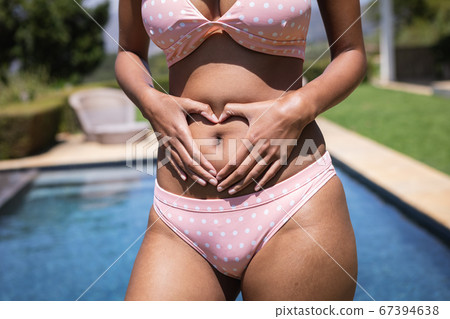 Mid section of woman holding her hands in heart shape on her stomach Mid section of woman holding her hands in heart shape on her stomach 67394638