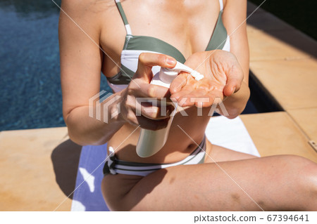 Mid section of woman using sunscreen while sitting by the pool 67394641
