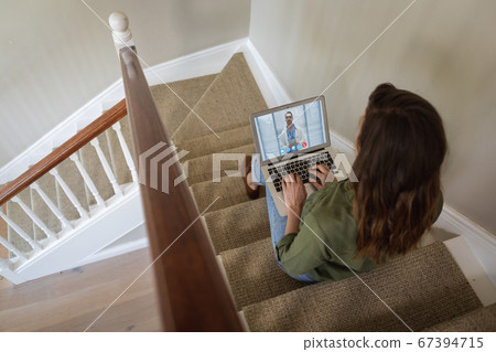 Woman having a video meeting on her laptop while sitting on staircase Woman having a video meeting on her laptop while sitting on staircase 67394715