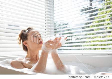 Woman blowing soap bubbles in a bathtub Woman blowing soap bubbles in a bathtub 67394753