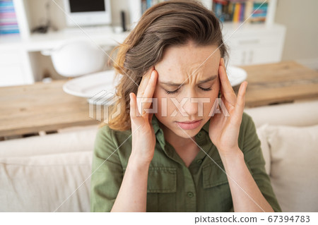 Woman with headache touching her head at home 67394783