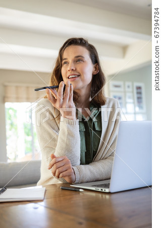 Woman with laptop talking on smartphone at home 67394784