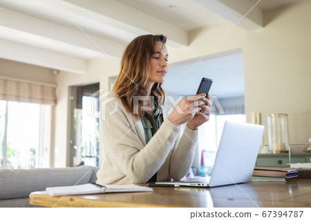 Woman with laptop using smartphone at home Woman with laptop using smartphone at home 67394787