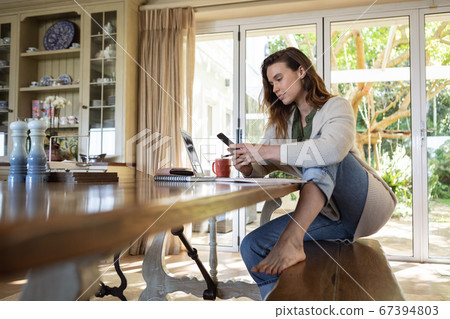 Woman with laptop using smartphone at home Woman with laptop using smartphone at home 67394803