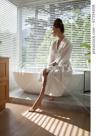 Woman in bathrobe sitting on bathtub Woman in bathrobe sitting on bathtub 67394806