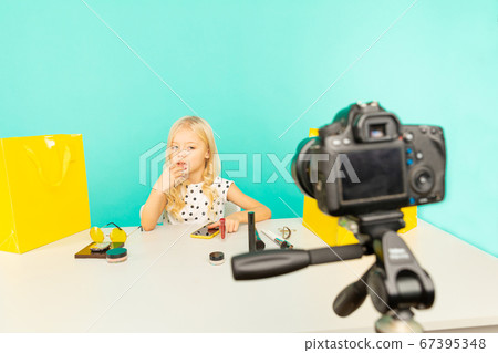 Happy girl sitting at the desk in the blue studio speaking in front of camera for vlog. Young beauty blogger recording video tutorial for Internet. 67395348