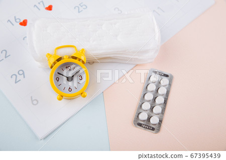 Menstrual calendar with pads, alarm clock and contraceptive pills. Menstruation period concept. Pain reliever for menstrual pain 67395439