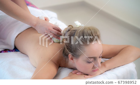 Massage therapist using herbal compress with woman 67398952